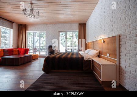 Une chambre confortable avec un grand lit avec une couverture brune, des meubles en bois et de grandes fenêtres permettant la lumière naturelle, complétée par un seati élégant Banque D'Images