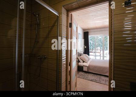Chambre confortable avec vue depuis la salle de bains, comprenant un lit, une fenêtre et une douche. Banque D'Images