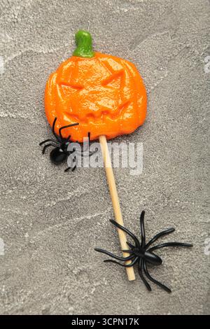 Sucettes d'Halloween en forme de citrouille avec araignée décorative sur fond de béton gris. Vue de dessus Banque D'Images