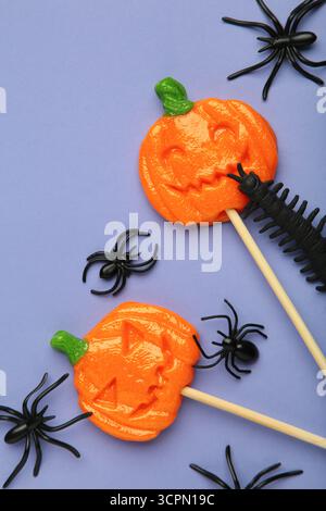 Sucettes d'Halloween en forme de citrouille avec araignée décorative sur fond violet. Gâteries festives pour les fêtes de fin d'année. Vue de dessus Banque D'Images