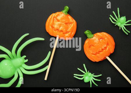 Sucettes d'Halloween en forme de citrouille avec araignée décorative sur fond noir. Gâteries festives pour les fêtes de fin d'année. Vue de dessus Banque D'Images