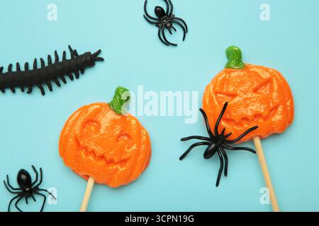 Sucettes d'Halloween en forme de citrouille avec araignée décorative sur fond bleu. Gâteries festives pour les fêtes de fin d'année. Vue de dessus Banque D'Images