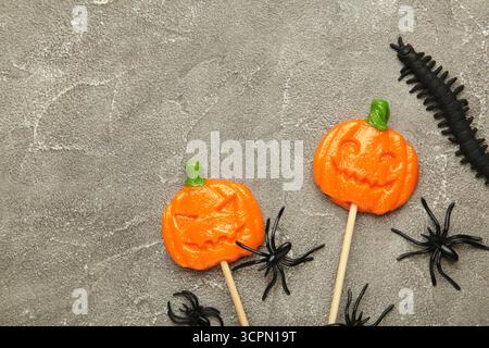 Sucettes d'Halloween en forme de citrouille avec araignée décorative sur fond de béton gris. Vue de dessus Banque D'Images