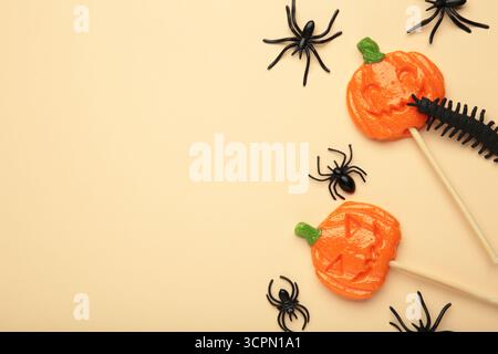Sucettes d'Halloween en forme de citrouille avec araignée décorative sur fond beige. Gâteries festives pour les fêtes de fin d'année. Vue de dessus Banque D'Images