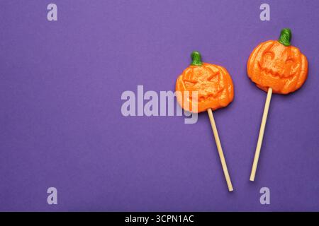 Sucettes d'Halloween en forme de citrouille sur fond violet. Gâteries festives pour les fêtes de fin d'année. Vue de dessus Banque D'Images