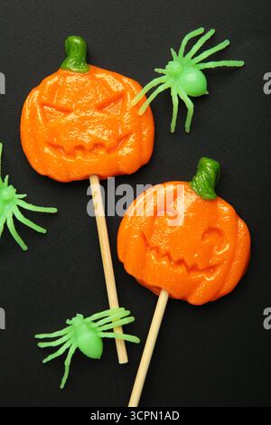Sucettes d'Halloween en forme de citrouille avec araignée décorative sur fond noir. Gâteries festives pour les fêtes de fin d'année. Vue de dessus Banque D'Images