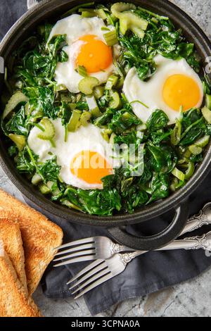 Shakshuka vert sain avec œufs, épinards, céleri, oignon, poivron vert et herbes gros plan dans une poêle sur la table. Vue de dessus verticale Banque D'Images
