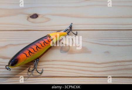 Gros plan d'un leurre de pêche d'eau douce orange vif et jaune reposant sur une surface en bois. Banque D'Images