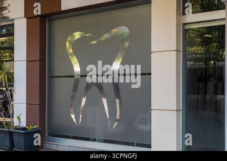 Un grand symbole de dent est affiché sur une fenêtre en verre dépoli d'une clinique dentaire dans une ville animée. La lumière du soleil illumine les environs Banque D'Images