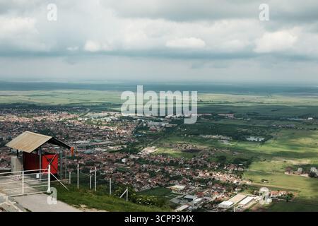 Vue panoramique sur la ville de Vrsac avec un ciel nuageux et les terres agricoles vertes environnantes, vues du sommet d'une colline. Au loin, vous pouvez voir les toits en tuiles rouges. Banque D'Images