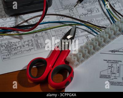 Fils du multimètre de travail électronique vue Zenith - vue de haut en bas d'un multimètre, d'un bornier, d'une pince coupante et de fils sur des schémas électroniques complexes. Repré Banque D'Images