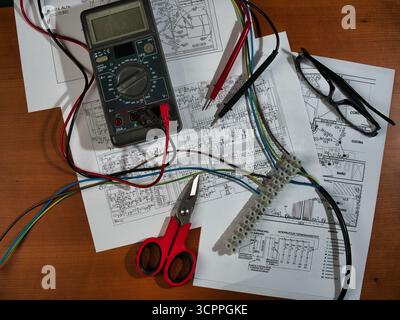 Fils du multimètre de travail électronique vue Zenith - vue de haut en bas d'un multimètre, d'un bornier, d'une pince coupante et de fils sur des schémas électroniques complexes. Repré Banque D'Images
