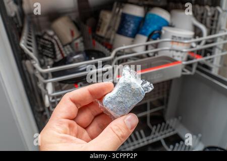 Allemagne - 27 septembre 2025 : une pastille de lave-vaisselle est tenue dans la main avant de commencer. En arrière-plan, le lave-vaisselle est chargé de tasses et de vaisselle, prêts pour le processus de nettoyage. *** Ein Spülmaschinentab wird vor dem Start in der hand gehalten. IM Hintergrund ist der beladene Geschirrspüler mit Tassen und Geschirr zu sehen bereit für den Reinigungsvorgang. Banque D'Images