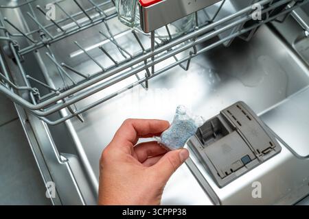 Allemagne - 27 septembre 2025 : une main tient une pastille de lave-vaisselle au-dessus du lave-vaisselle ouvert. Le compartiment distributeur est visible et indique la prochaine étape de chargement du produit de lavage. *** Eine hand hält einen Spülmaschinentab über der geöffneten Spülmaschine. DAS Dosierfach ist sichtbar und zeigt den nächsten Schritt beim Einlegen des Reinigungsmittels. Banque D'Images
