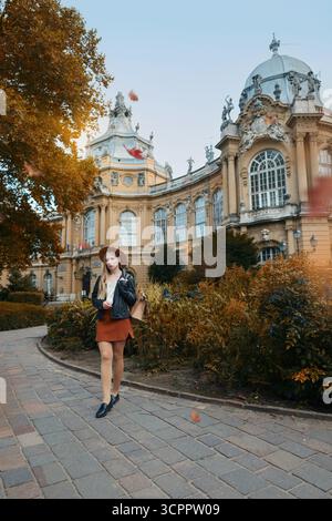 Jeune femme en veste en cuir et jupe profitant du voyage près du château médiéval. Banque D'Images