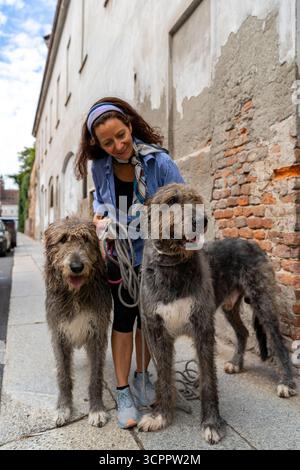 Femme et deux grands chiens de loup irlandais debout sur le trottoir, regardant la caméra Banque D'Images
