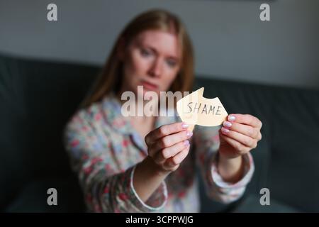 Femme triste tenant une note avec le mot honte, symbolisant la culpabilité, la stigmatisation et la lutte émotionnelle. Banque D'Images