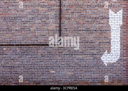 Un mur de briques avec un tuyau et une flèche blanche. Banque D'Images