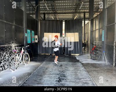 Un homme couvre un vélo avec de la mousse dans un lave-auto en libre-service. Bichkek, Kirghizistan - 25 septembre 2025 Banque D'Images