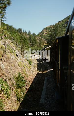 Train vintage courbant à travers un paysage de montagne pittoresque à Mokra Gora, entouré de pins et de terrains rocheux. Sargan huit - un touriste populaire Banque D'Images