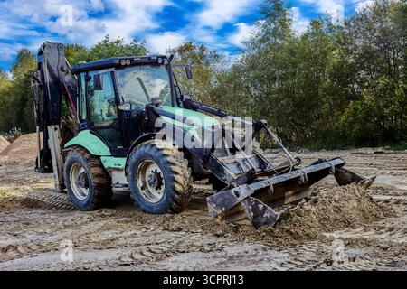 Le chargeur frontal effectue des travaux sur site avec des tas de sable présents sur la zone de travail. Banque D'Images