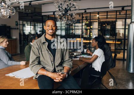 Portrait of smiling businessman sitting on desk in office Banque D'Images