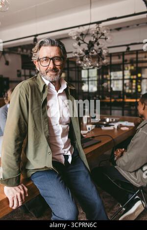Portrait de souriant expert masculin en affaires portant des lunettes assis sur la table dans le bureau Banque D'Images