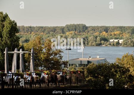 Terrasse de café en plein air à Belgrade avec tables et parasols fermés donnant sur le Danube et la forêt verte en arrière-plan. Banque D'Images
