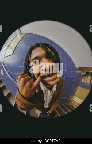 Fish Eye Lens portrait d'un jeune homme ludique avec le doigt dans la bouche debout sur les marches du métro Banque D'Images