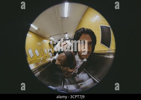 Fish Eye Lens portrait d'un jeune homme portant sac à dos debout sur l'escalator avec des amis dans le métro Banque D'Images