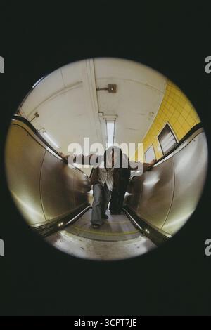 Fish Eye Lens portrait d'un jeune homme se penchant tout en se déplaçant sur l'escalator dans le métro Banque D'Images