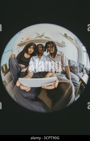 Jeune homme prenant selfie avec des amis par téléphone intelligent tout en étant assis sur le lit à la maison dans Fish Eye photo Banque D'Images
