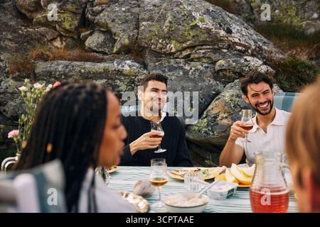 Heureux amis mâles buvant du vin tout en profitant du dîner pendant les vacances d'été Banque D'Images