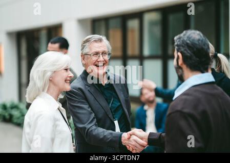 Heureux entrepreneur masculin sénior serrant la main d'un collègue au centre des congrès Banque D'Images