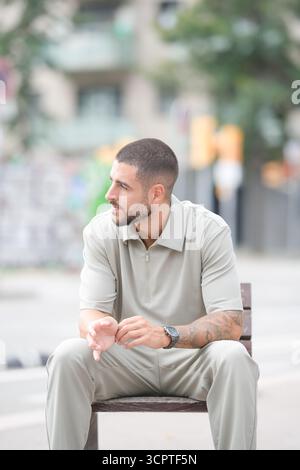 Un homme est assis sur un banc dans une rue de la ville. Il porte une chemise et un pantalon et a une montre au poignet. La scène est calme et paisible, avec l'homme lo Banque D'Images
