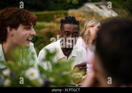 Homme souriant parlant avec un ami tout en profitant du dîner dans la cour arrière Banque D'Images