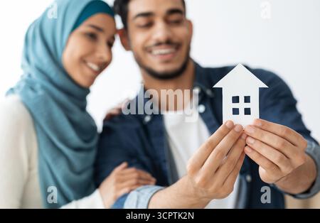 Jeune couple musulman tenant une maison de papier et souriant Banque D'Images