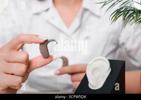 Les prothèses auditives numériques modernes dans les mains de l'audiologiste en clinique. Médecin tenant une prothèse auditive, modèle près de l'oreille pour l'ajustement et la démonstration. Gros plan Banque D'Images