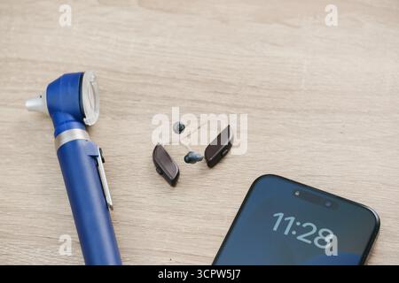 Vue de dessus minimaliste des aides auditives numériques modernes, otoscope et smartphone sur un bureau en bois. Mise en page propre en audiologie ou en contexte de soins auditifs. Copier Banque D'Images