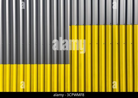 Mur ondulé industriel avec des lignes verticales, moitié peinte en gris et moitié en jaune vif, créant un contraste géométrique symétrique audacieux Banque D'Images