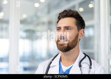 Médecin masculin souriant en blouse de laboratoire blanche avec stéthoscope, confiant et accessible, travaillant dans une clinique moderne lumineuse cadre professionnel, attentionné et digne de confiance clinicien Banque D'Images