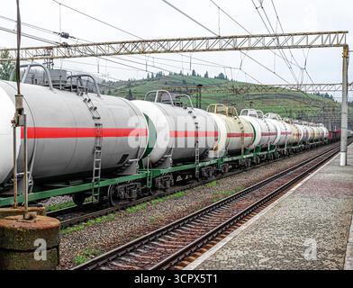 Un train de marchandises industriel avec des wagons-citernes transportant des marchandises liquides est stationné sur des voies ferrées dans une station de montagne Banque D'Images