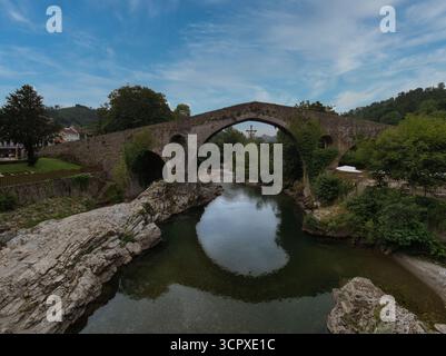Pont de pierre médiéval historique au-dessus de la rivière - pittoresque pont de pierre à une seule arche avec un lierre épais traversant une rivière calme et réfléchissante entourée d'une végétation luxuriante Banque D'Images