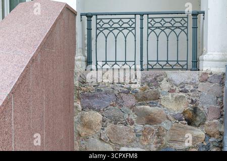 Une composition d'éléments architecturaux : une vieille fondation en pierre brute, un mur de granit moderne et élégant et une balustrade décorative en fer forgé. Banque D'Images