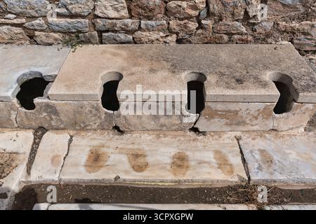 Latrines publiques des bains Scholastica, Ephèse, Selcuk, Turquie. Toilettes romaines anciennes en pierre communales avec plusieurs trous. Site archéologique historique Banque D'Images