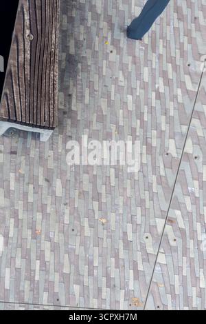 Vue rapprochée de haut en bas d'un sol ou d'une surface en miroir reflétant un motif de pavage gris texturé et une partie d'un banc en bois. Banque D'Images