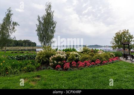 Un grand plan d'un parterre de fleurs magnifiquement entretenu avec diverses fleurs, séparant une pelouse verte luxuriante de l'eau calme du lac au-delà. Banque D'Images