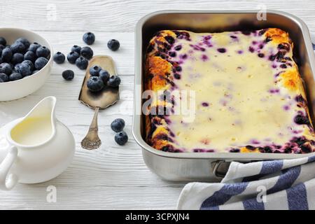 Mustikkapiirakka, tarte finlandaise aux myrtilles dans un plat de cuisson sur une table en bois blanc avec une pelle à gâteau et des ingrédients, vue horizontale d'en haut, pas de gène IA Banque D'Images
