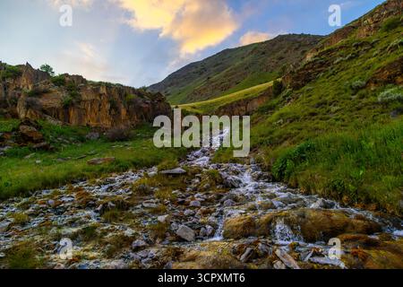 Ruisseau tranquille coule doucement sur des roches lisses dans une région montagneuse majestueuse du Kirghizistan Banque D'Images