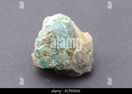 Un échantillon minéral rugueux et multicolore avec des nuances de vert, blanc et bronzé est placé au centre sur un fond gris foncé lisse. Appelé Dioptas. Banque D'Images